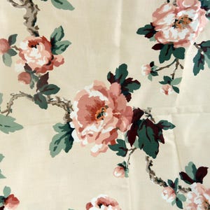 May include: Cream-colored fabric with a repeating floral pattern. Large, open pink and white flowers with dark green leaves and brown stems are scattered across the surface. The design evokes a vintage or cottagecore aesthetic.