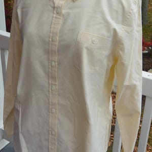 Puede incluir: Camisa abotonada de color amarillo p&aacute;lido con cuello abotonado y bolsillo en el pecho. La camisa de manga larga tiene un dise&ntilde;o cl&aacute;sico con botones en la parte delantera y en los pu&ntilde;os. La camisa se exhibe en un maniqu&iacute;.