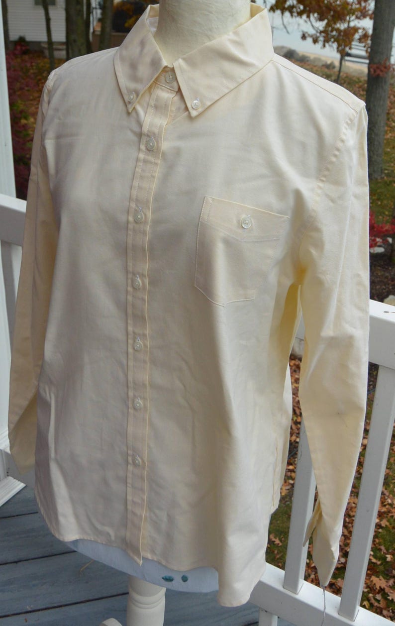 Puede incluir: Camisa abotonada de color amarillo p&aacute;lido con cuello abotonado y bolsillo en el pecho. La camisa de manga larga tiene un dise&ntilde;o cl&aacute;sico con botones en la parte delantera y en los pu&ntilde;os. La camisa se exhibe en un maniqu&iacute;.