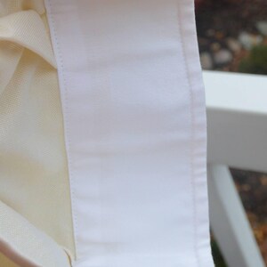 Puede incluir: Primer plano de un cuello de camisa blanco con un interior crema contrastante. El cuello tiene dos ojales y est&aacute; hecho de una tela suave y crujiente. Los bordes est&aacute;n cuidadosamente acabados con un sutil ribete de color claro. El fondo est&aacute; borroso.