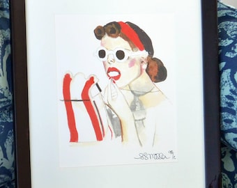 May include: Framed watercolor painting of a woman applying lipstick, wearing a red headband and white sunglasses. The artwork features a retro style with bold red and white accents. The painting is signed by the artist.