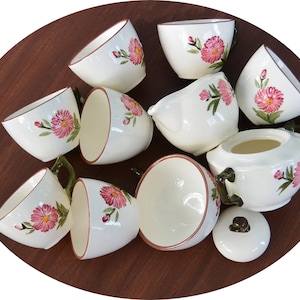 May include: A set of white ceramic teacups and saucers with pink floral designs. The set includes a teapot, sugar bowl, and creamer.