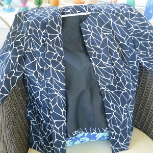 Op de afbeelding: Een blazer met lange mouwen met een donkerblauwe basis en een wit geometrisch patroon dat doet denken aan gebarsten steen of mozaïektegels. Het kledingstuk heeft een effen zwarte binnenvoering en een rechte opening aan de voorzijde.