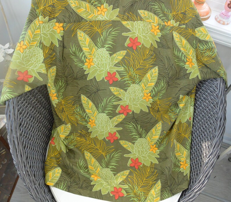 K&ouml;nnte beinhalten: Gr&uuml;nes Hemd mit Kn&ouml;pfen und tropischem Blumenmuster. Das Hemd hat ein sich wiederholendes Design aus gro&szlig;en gr&uuml;nen Blumen, orangefarbenen und gelben Akzenten sowie farnartigen Bl&auml;ttern. Hergestellt aus leichtem Stoff, ideal f&uuml;r warmes Wetter.