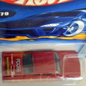 May include: A red die-cast toy car with the text "FOOSE" and "MAGNAFLOW" on the side. The car is packaged in a clear plastic blister pack with a blue and yellow background featuring a stylized car.