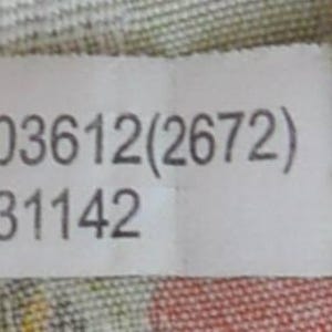 K&ouml;nnte beinhalten: Ein wei&szlig;es Etikett mit dem Text "P0803612(2672)" und "61-T31142" in Grau. Das Etikett befindet sich vor einem gemusterten Stoffhintergrund mit Orange- und Gr&uuml;nt&ouml;nen.