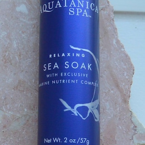 May include: A blue cylindrical bottle of "AQUATANICA SPA" Sea Soak. The label includes the words "RELAXING SEA SOAK" and "WITH EXCLUSIVE MARINE NUTRIENT COMPLEX". The bottle contains 2 oz / 57g of product.