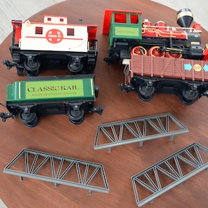 以下が含まれることがあります： 赤い、緑、黒の機関車、緑色の貨車には「Classic Rail」と「Rocky Mountain Express」の文字が印刷され、白い貨車には「Santa Fe」の文字が印刷され、茶色の貨車には「SP」の文字が印刷されたおもちゃの列車セット。このセットには、灰色の金属製の橋が2つ含まれています。