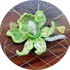 May include: A vibrant green and pink enamel flower brooch with a sparkling rhinestone center and stem. The brooch is a detailed floral design, perfect for adding a touch of color and elegance to any outfit. The brooch is a unique piece of jewelry.