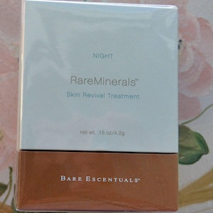 May include: A rectangular box of BareMinerals Skin Revival Treatment. The top half is light gray with the word "NIGHT" and "RareMinerals" printed in black. The bottom half is brown with the words "BARE ESCENTUALS" printed in white. Net weight is .15 oz/4.2g.