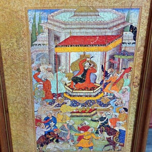 May include: A framed jigsaw puzzle depicting a historical scene with figures in colorful attire. The central figure, in red, is seated under a canopy. The puzzle is framed in a dark wood.