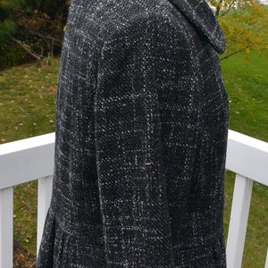 May include: A black and white tweed jacket with a collar and a ruffled hem. The jacket is on a white mannequin.
