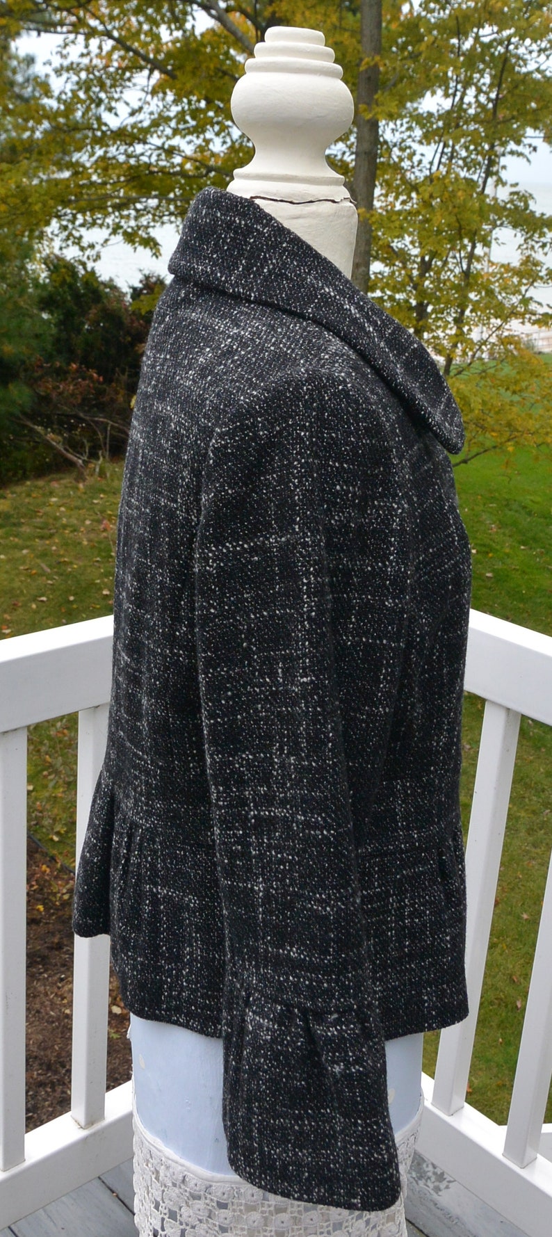 May include: A black and white tweed jacket with a collar and a ruffled hem. The jacket is on a white mannequin.