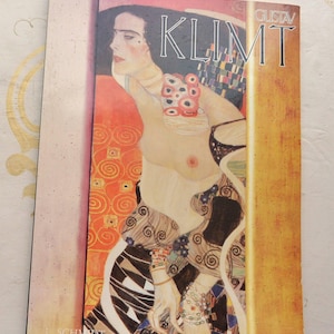 May include: A book cover featuring Gustav Klimt's artwork. The cover displays a partial nude portrait with intricate patterns in gold, orange, and black. The title "KLIMT" is prominently displayed in white, with the artist's name above.