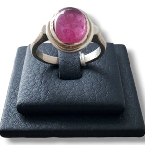 May include: A silver ring with a pink oval gemstone set in a bezel setting. The ring is displayed on a black ring display stand.
