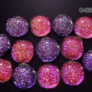 May include: An assortment of iridescent, glittery cabochons in shades of purple, pink, and gold. The cabochons are arranged on a black background. The text "0420" is visible in the upper right corner. These could be used for jewelry making or other crafts.