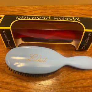 May include: A light blue hairbrush with black bristles and the name "Lisa" written in gold lettering. The brush is in a box with the words "Mason Pearson London England" on the front.