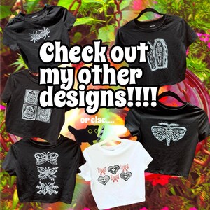 May include: Five black crop tops with different graphic designs. The designs include a spider, a coffin, a moth, a butterfly, and a series of squares. The text "Check out my other designs!!!" is superimposed on the image.