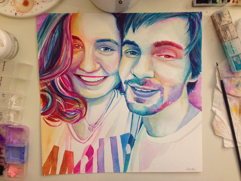 Pode incluir: Pintura em aquarela de um casal, uma mulher com cabelo longo rosa e um homem com cabelo azul, ambos sorrindo. A pintura &eacute; feita em um estilo vibrante com respingos de cor.