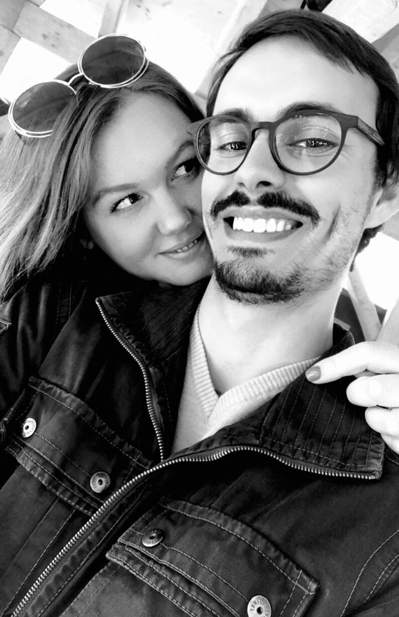 May include: A black and white photo of a couple smiling. The man is wearing a black jacket and glasses. The woman is wearing a jacket and sunglasses.