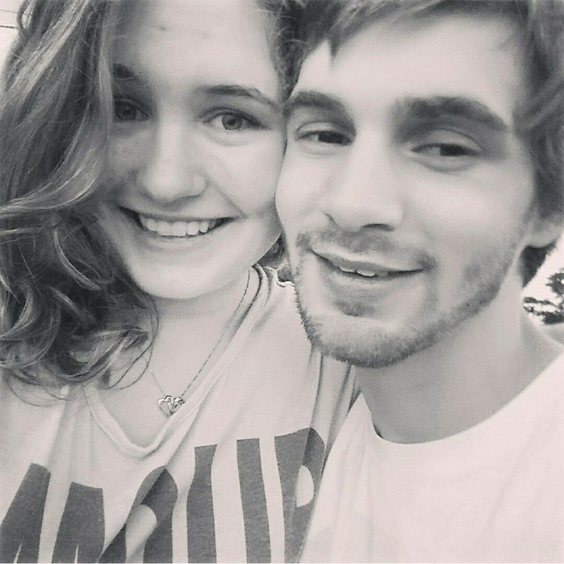 Pode incluir: Uma fotografia a preto e branco de um casal a sorrir para a c&acirc;mara. A mulher est&aacute; a usar uma camisa branca com um padr&atilde;o de riscas pretas e brancas. O homem est&aacute; a usar uma camisa branca.