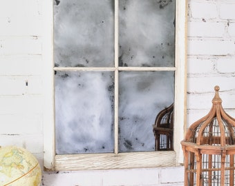 May include: A white painted wood framed mirror with four panes of glass. The mirror has a distressed look with a cloudy, aged appearance. The mirror is hanging on a white brick wall.