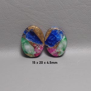 May include: Two oval-shaped cabochons featuring a mosaic pattern of blue, green, pink, and gold-toned segments. The stones measure 15 x 20 x 4.5mm as indicated by the text printed below the items on the surface.