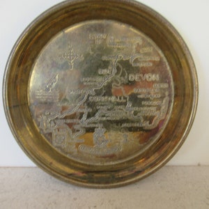 Puede incluir: Una bandeja de metal dorado con un mapa de Cornualles y Devon, Inglaterra. La bandeja incluye el texto "Cornwall" y "Devon" junto con los nombres de varias ciudades y pueblos de la región.