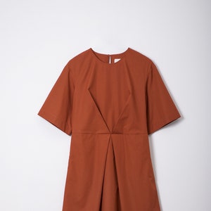 May include: A rust-coloured short-sleeved dress with a V-shaped neckline and a pleated skirt.