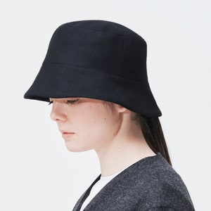 Puede incluir: Un sombrero de cubo negro de fieltro con un ala ancha y un diseño sencillo.