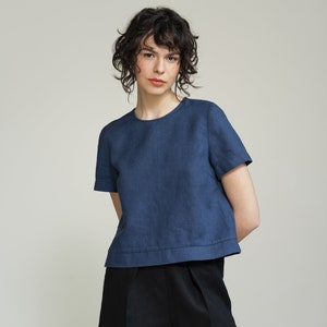 K&ouml;nnte beinhalten: Eine Frau tr&auml;gt ein blaues Leinenoberteil mit kurzen &Auml;rmeln und eine schwarze Leinenhose.