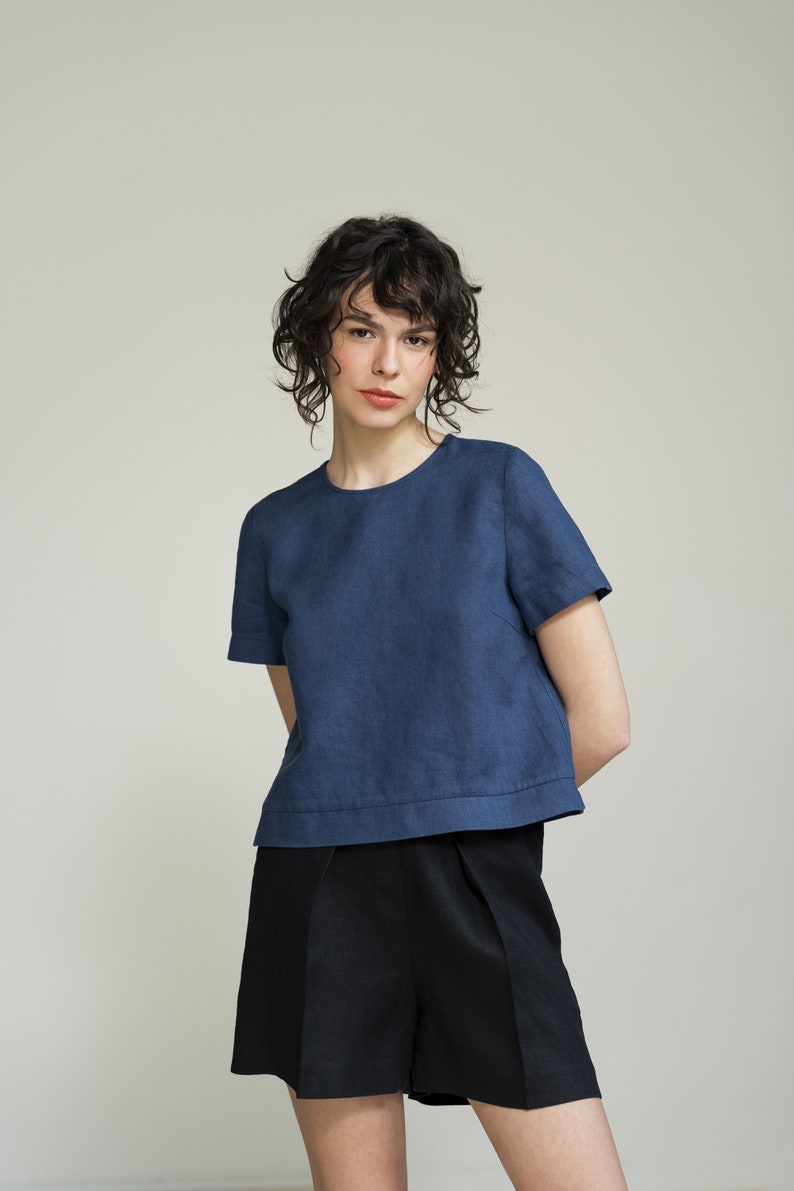 K&ouml;nnte beinhalten: Eine Frau tr&auml;gt ein blaues Leinenoberteil mit kurzen &Auml;rmeln und eine schwarze Leinenhose.