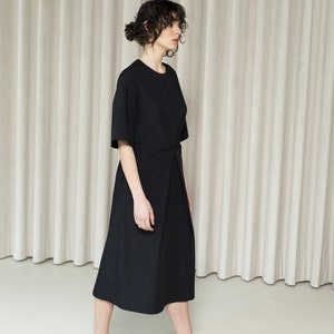 May include: A woman wearing a black midi dress with a knot detail at the waist and black sandals.