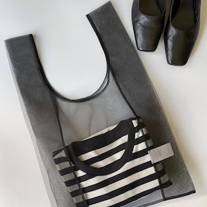 May include: A black mesh tote bag with a black and white striped shirt inside, and a pair of black leather Mary Jane style shoes with square toes. The items are arranged on a white surface.