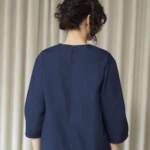 K&ouml;nnte beinhalten: Eine dunkelblaue Bluse mit Dreiviertel&auml;rmeln, Rundhalsausschnitt und Knopfleiste im R&uuml;cken.