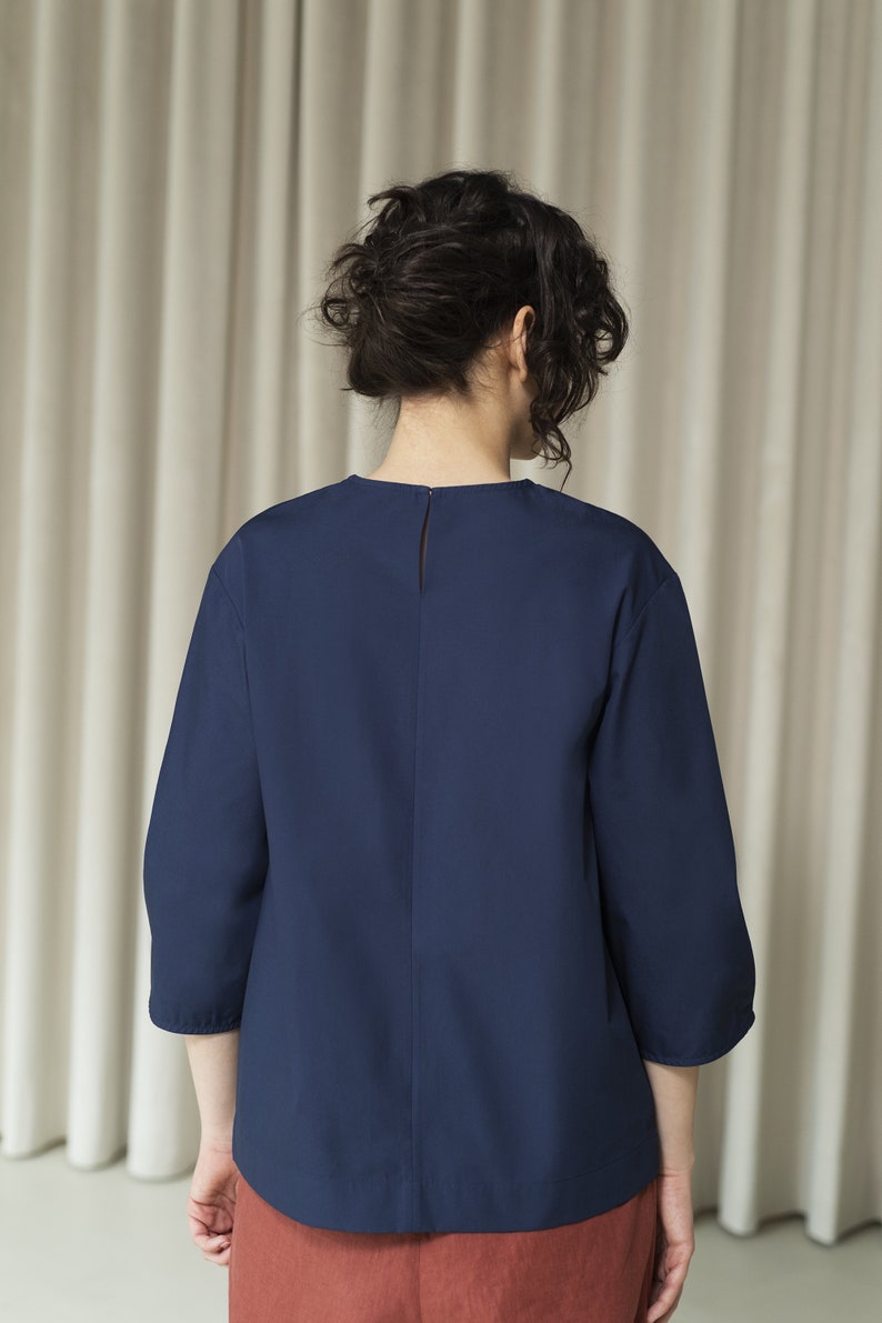 K&ouml;nnte beinhalten: Eine dunkelblaue Bluse mit Dreiviertel&auml;rmeln, Rundhalsausschnitt und Knopfleiste im R&uuml;cken.
