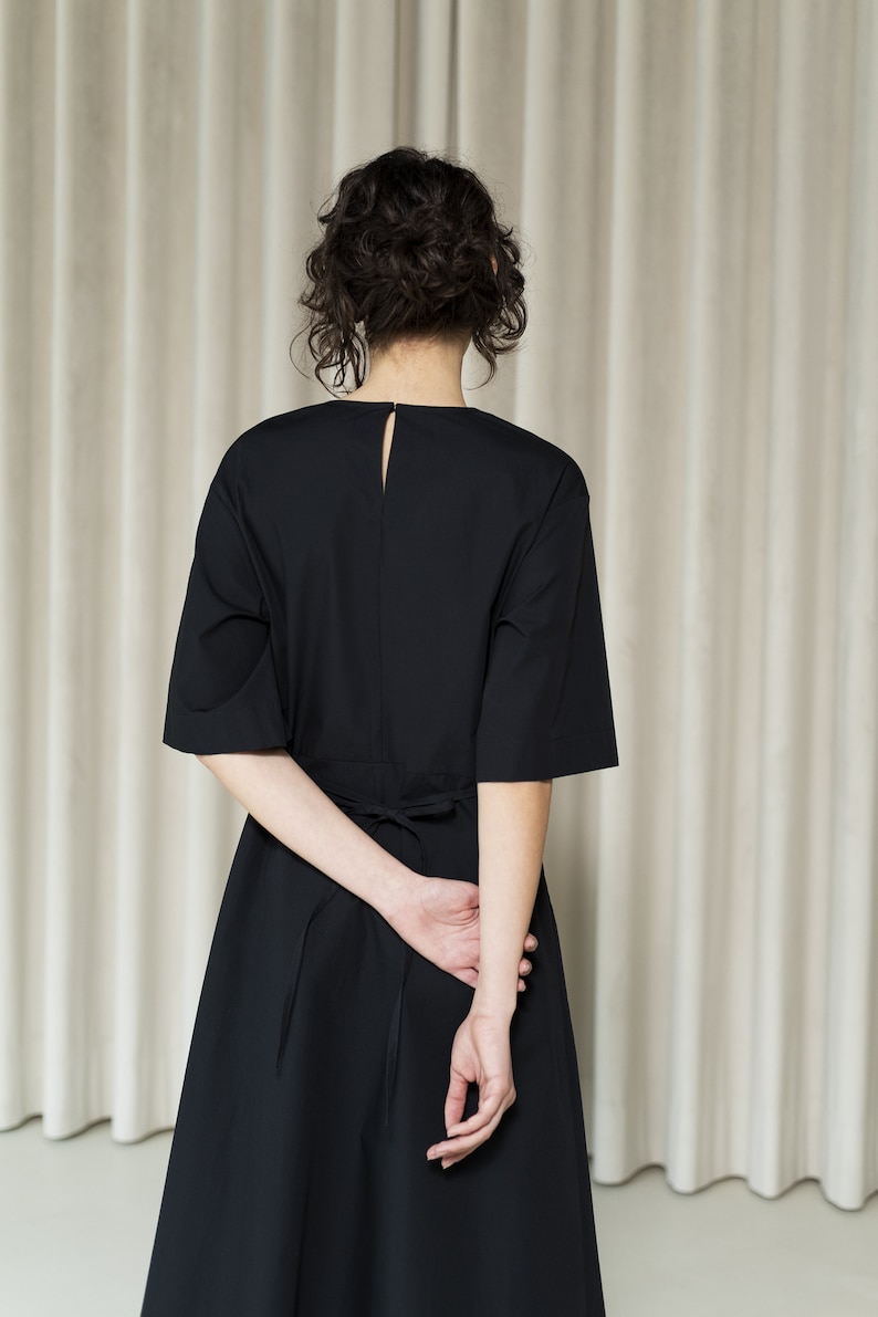 May include: A black midi dress with a tie at the waist. The dress has a simple, elegant design and is perfect for a variety of occasions.