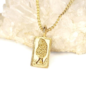 May include: A gold chain necklace with a rectangular pendant featuring a detailed mushroom design. The necklace is displayed on a bed of clear quartz crystals.