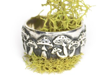 May include: A silver ring with a mushroom design. The ring is surrounded by green moss.