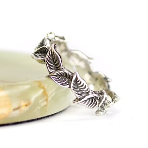 May include: A silver ring with a delicate design of leaves encircling the band.