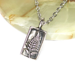 May include: A silver necklace with a rectangular pendant featuring an embossed fern design.