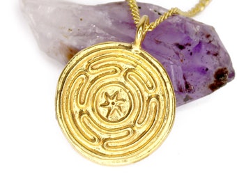 May include: A gold necklace with a circular pendant featuring a detailed labyrinth design and a star in the center. The pendant is resting on a purple amethyst crystal.