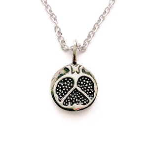 May include: Silver-toned necklace featuring a pendant shaped like a pomegranate. The pendant has a detailed design of the fruit's interior, with a textured surface. The chain is a classic link style, and the background is white.