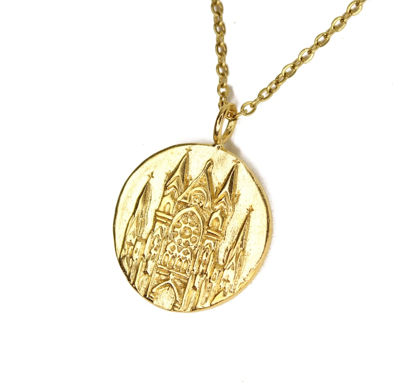 May include: A gold necklace with a round pendant featuring a detailed embossed design of a church building.