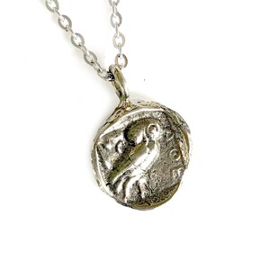 May include: Silver necklace with a round pendant featuring a detailed embossed design of a bird. The pendant has a textured, aged look.