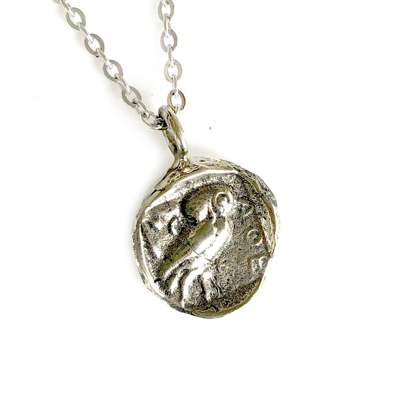 May include: Silver necklace with a round pendant featuring a detailed embossed design of a bird. The pendant has a textured, aged look.