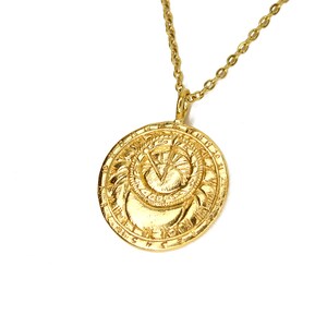 May include: A gold necklace with a round pendant featuring a detailed design of a sun and moon with Roman numerals around the edge.