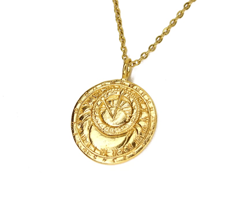 May include: A gold necklace with a round pendant featuring a detailed design of a sun and moon with Roman numerals around the edge.