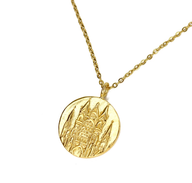 May include: A gold necklace with a round pendant featuring a detailed embossed design of a cathedral.