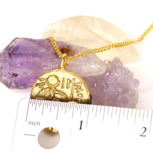 May include: Gold necklace with a round pendant featuring an Egyptian hieroglyphic design. The pendant is about 1 inch in diameter and is resting on a purple amethyst crystal.